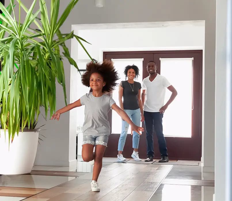 A happy child running through the front door as her parents watch on with satisfaction and delight