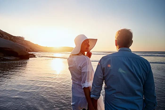 Couple holding hands on the beach at sunset, with the ocean in the background