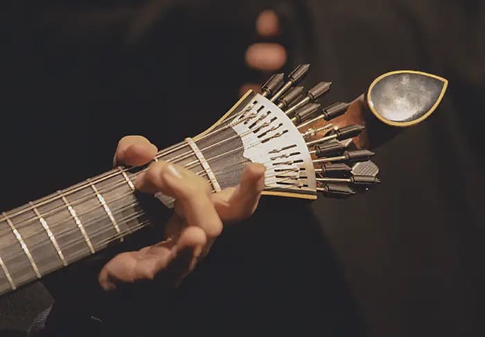 Close-up of hands playing a Portuguese guitar, focusing on the headstock and tuning pegs