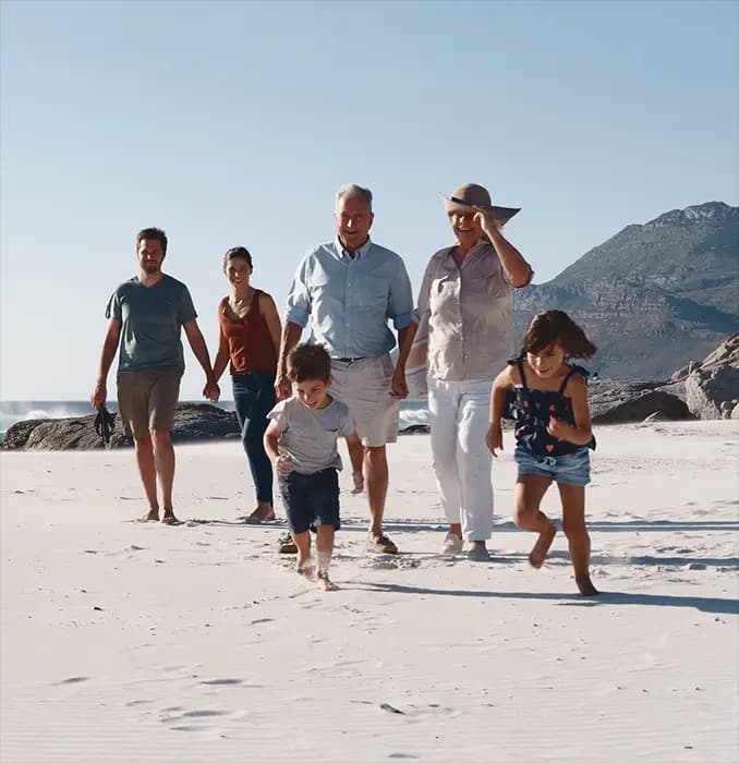 Family walking on a sandy beach as children run ahead, mountains in the background