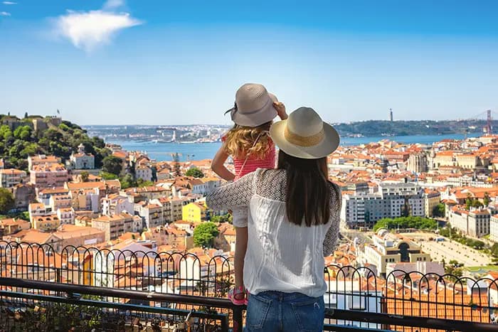 Woman and child in sun hats overlooking Lisbon’s rooftops and the Tagus River from a Graça district viewpoint
