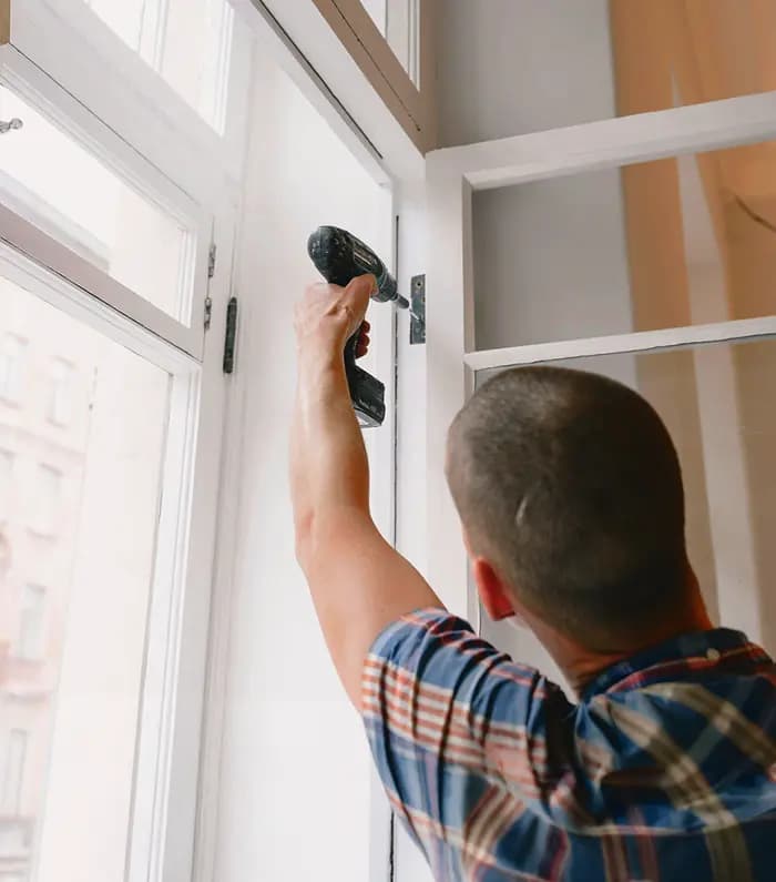 A tradesman fixing a window hing with an electric screwdriver